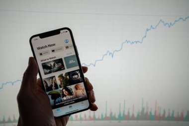 Telefondaki Apple TV uygulaması beyaz finansal tablolu ve arka planda yükselen fiyat artışı pozitif