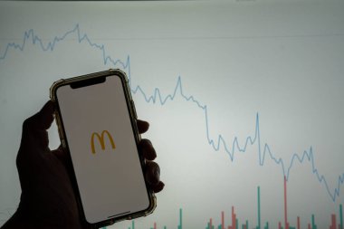 McDonald 's mobil uygulama logosu iPhone' da beyaz borsa grafiği önünde sağa doğru değer kaybediyor.