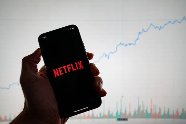 Netflix app on phone with white financial stock chart with price rising upward positive in background — Stock Photo, Image