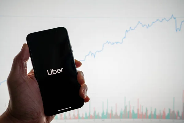 Uber app on phone with white financial stock chart with price rising upward positive in background — Stock Photo, Image