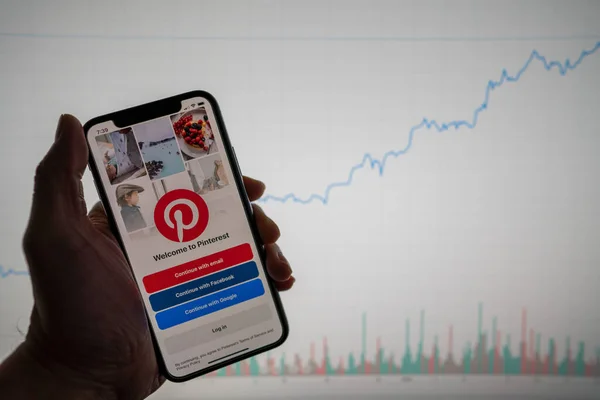 Pinterest app on phone with white financial stock chart with price rising upward positive in background — Stock Photo, Image