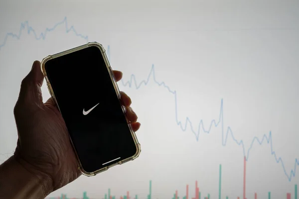 Nike mobile app logo on iPhone in front of white stock market chart with graph going down in value — Stock Photo, Image