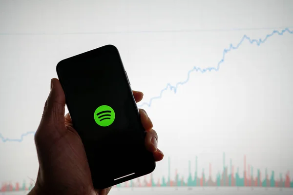 Spotify aplicación en el teléfono con blanco gráfico de acciones financieras con el aumento de los precios al alza positiva en segundo plano Imagen De Stock
