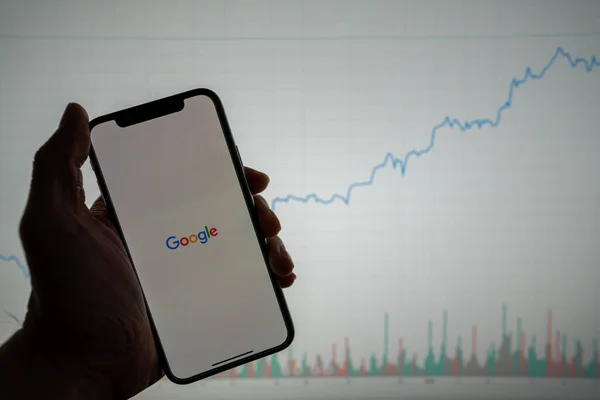 Logo Google sur téléphone avec graphique financier blanc avec hausse des prix positive en arrière-plan Image En Vente