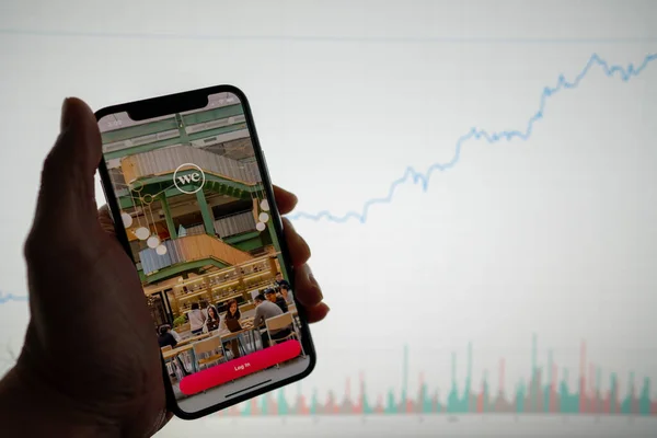 Aplicación y logotipo de WeWork en el teléfono con gráfico de acciones financieras blancas con un aumento de precios positivo en segundo plano Imagen De Stock