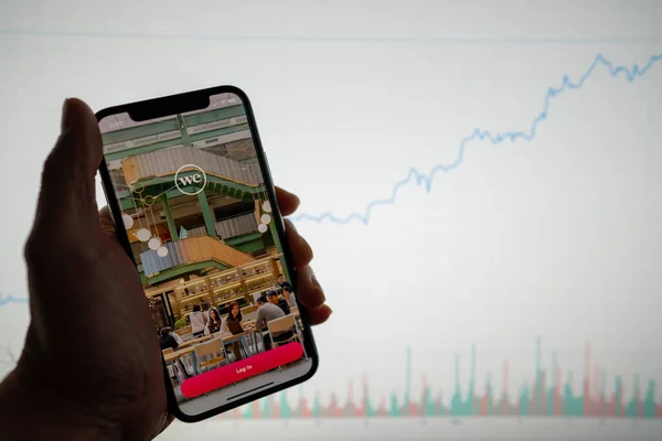 Application WeWork et logo sur téléphone avec graphique financier blanc avec hausse des prix positive en arrière-plan Photo De Stock