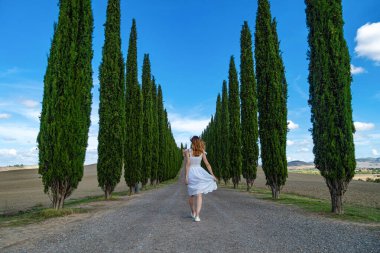 Beyaz elbiseli kadın Cypress Trees sıralarıyla yolda yürüyor