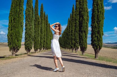 Beyaz elbiseli kadın Cypress Trees sıralarıyla yolda yürüyor