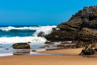 Kumlu bir sahilde dalgalanan okyanus dalgaları.