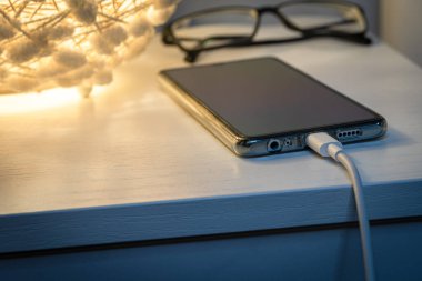 Akşamları komodinin üzerinde enerji bankasıyla şarj olan akıllı telefon. Telefon şarj cihazına bağlandı