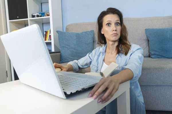 Young wondered woman works for a computer from a home with a laptop on a white desk as a freelancer