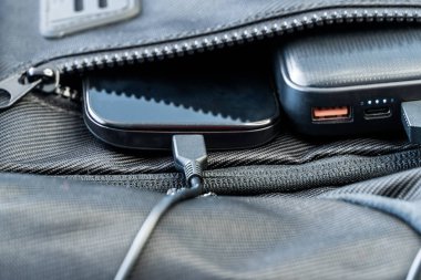 Sırt çantasında siyah enerji bankasıyla şarj olan akıllı telefon, seçici odaklı