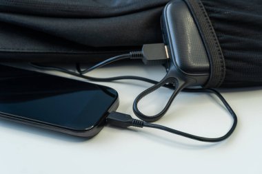 Beyaz tahta üzerinde sırt çantasında enerji bankasıyla şarj olan akıllı telefon. Telefon şarj cihazına bağlandı