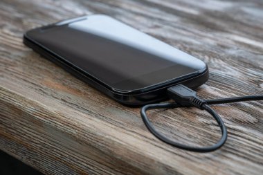 Tahta masada elektrik bankasıyla şarj olan akıllı telefon. Telefon şarj cihazına bağlandı