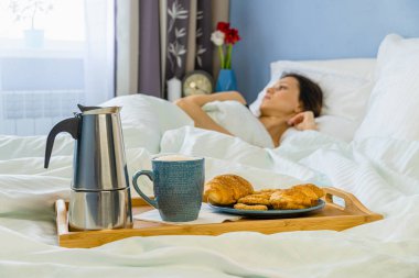 Yatak odasındaki güzel kadın için tepside hamur işleriyle yatak ve kahvaltı.