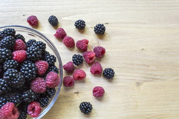 Raspberries and blackberries in a glass jar on a wooden table. — Stock Photo, Image