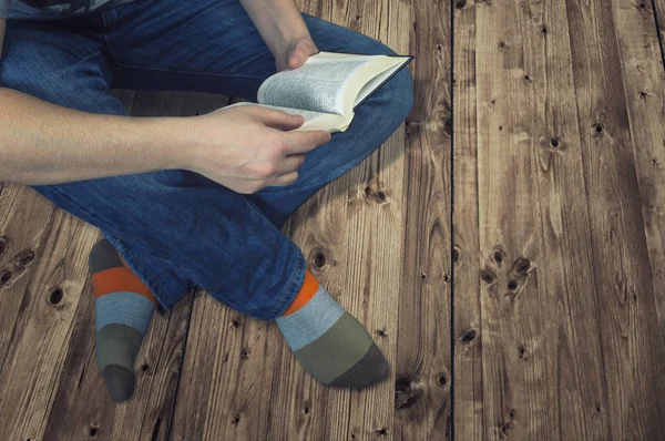 Женщина сидит на деревянном полу и читает книгу — стоковое фото
