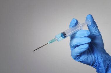 Hand in a blue glove holding a syringe.