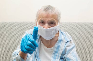 Yaşlı bir kadın hijyen maskesi ve koruyucu eldiven takarak COVID-19 'la kavga ettiği için baş parmağını kaldırıyor. Coronavirus koruma kavramı