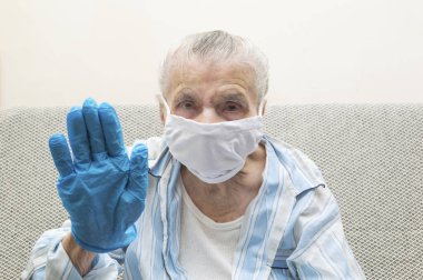 Tıbbi maskeli yaşlı bir kadın dur levhasında elini kaldırdı. Covid-19 virüs salgınını ve dünya çapında salgını durdurmak için ellerini kaldırdı. Coronavirus reddetme konsepti