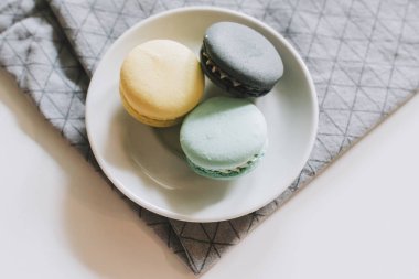 Basit bir beyaz tabakta sarı, gri ve nane maracons