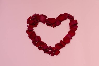 Pembe arka planda yalıtılmış gül yapraklarından oluşan kırmızı kalp
