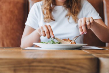 Beyaz tişörtlü, kıvırcık saçlı, salata ve tavuk yiyen genç bir kadın.