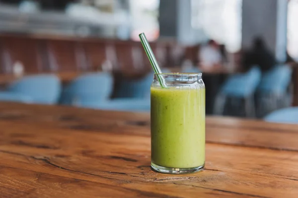 Glass with green healthy detox vegetarian smoothie drink on rough wooden table surface in a cafe or restaurant — Stock Photo, Image