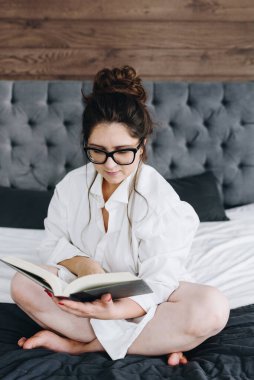 Genç, beyaz, seksi bir kadın sabahları yatak odasında kitap okuyor ve mesaj atmak için yeri var.