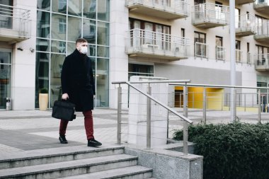 Karantina sırasında Coronavirus covid-19 'u korumak için cerrahi maske takarak evden işe giden beyaz bir genç.