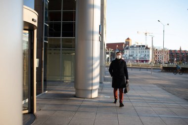 Coronavirus covid-19 covid 19 virüs salgınından korunmak için ameliyat maskesiyle ofisinin önünde yürüyen genç bir adam.