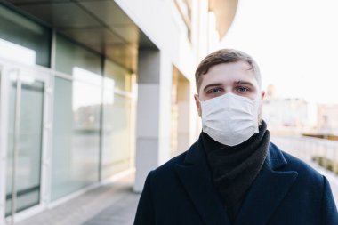 Coronavirus covid-19 virüsünden korunmak için ameliyat maskesi takan genç beyaz bir adam.