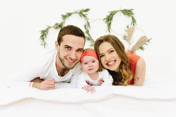 Familia caucásica de madre, padre y bebé sonriendo a la cámara en una cama — Foto de Stock