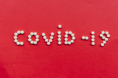 Küresel koronavirüs salgını sırasında kırmızı zemin üzerinde tabletlere veya haplara yazılmış Covid-19 veya covid 19
