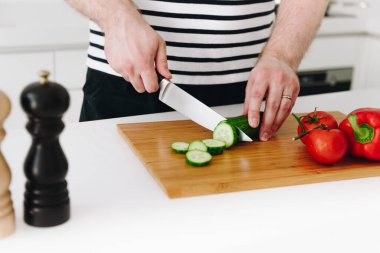 Modern beyaz bir mutfakta bıçakla güzel, sağlıklı bir sebze yemeği ya da salata pişiren beyaz bir adamın ellerine yakın durun.
