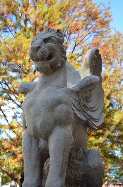 Estátua de um leão alado contra folhas de outono — Fotografia de Stock