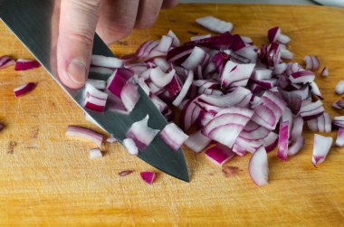 Bir adam mutfak bıçağıyla ahşap kesim tahtasına kırmızı soğan kesiyor. Eller yukarı. Yemek hazırlıyorum. Yan görünüm