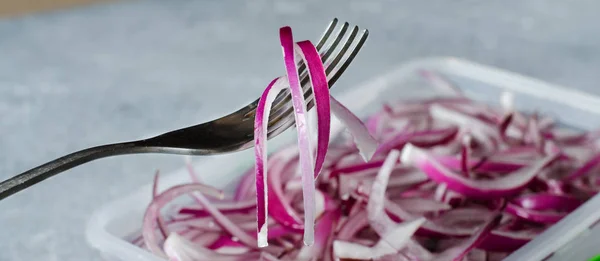 Pickled chopped red onion in vinegar in a plastic container. A delicious side dish for meat and fish dishes. Light grey background.