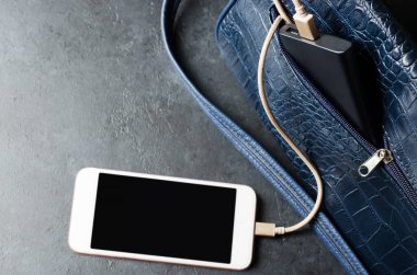 Blue Power Bank ve telefon kadınların çantasında. Koyu gri beton arka plan. Boşluğu kopyala