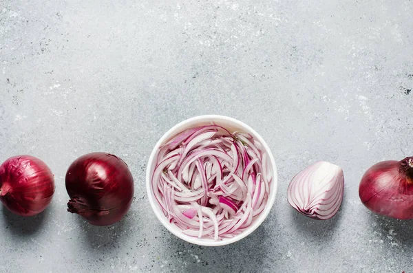 Pickled chopped red onion in vinegar in a white plate. Whole and sliced onions. A delicious side dish for meat and fish dishes. Light grey background. Flat top view