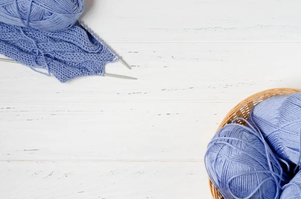 蓝色的纱线和针织针织在圆柳条筐里.白色的木制背景。编织- -女人的针线活。复制空间 — 图库照片