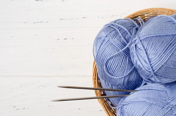 蓝色的纱线和针织针织在圆柳条筐里.白色的木制背景。编织- -女人的针线活。复制空间 — 图库照片