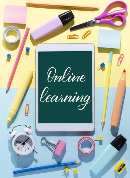 Çevrimiçi öğrenme - bir tablete el yazısıyla yazılmış yazı. Çocuklar için uzak mesafe eğitimi kavramı. Tablet ve ofis malzemeleri renkli bir arkaplanda