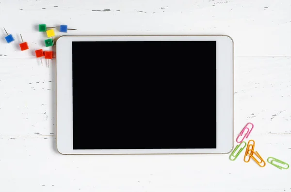 Boş ekranlı bir tablet ve beyaz ahşap arka planda ofis malzemeleri. Okul çocukları için konsept uygulaması ya da internetten öğrenme. Boşluğu kopyala