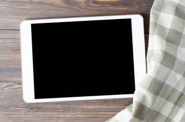 Kahverengi ahşap arka planda bir tablet bilgisayar ve bir masa örtüsü. Uzayı kopyala Yemek tarifi kavramı.