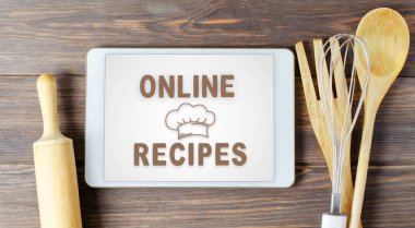 İnternette tarifler. Tablet bilgisayarda yemek kitabı. Mutfak aletleri. Kahverengi ahşap arka plan.