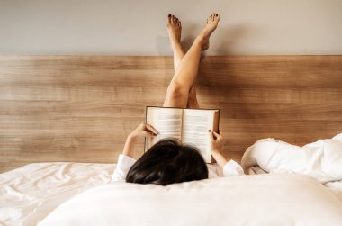 Asyalı bir kadın uzanmış, bacak bacak üstüne atmış, yatakta kitap okuyordu.