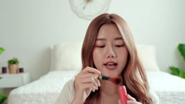  Güzel bir kadın yatak odasında makyaj fırçasıyla yüzünü kızartır. Asyalı kadın makyajını kendisi yapar..