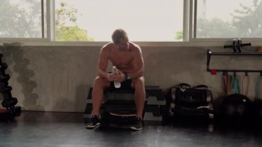 Spor salonunda egzersiz yapan yakışıklı bir delikanlının güzel vücut şekli. O dinleniyor ve pencerenin yanındaki spor salonunda su içiyor..