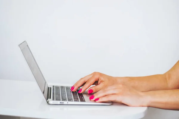 Female hands working on modern laptop. Close-up view of spectacles on notepad and person using laptop behind.